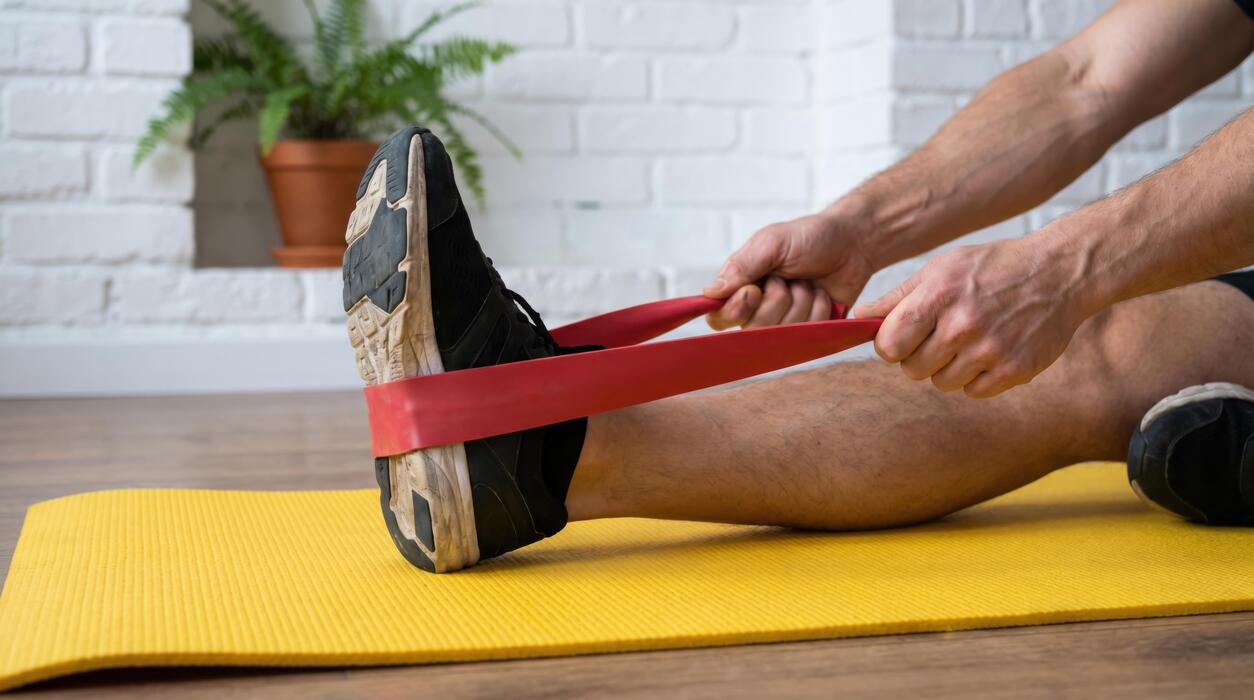 knee pain home remedies - Man stretching leg with red elastic band on yellow yoga mat at home