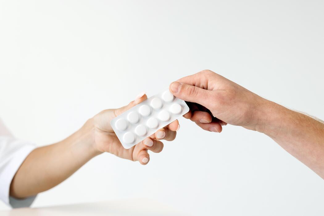 Kamagra Oral Jelly 100mg UK - Hands exchanging a blister pack of white pills, showcasing a healthcare interaction, with a soft blurred background emphasizing the importance of medication and patient care