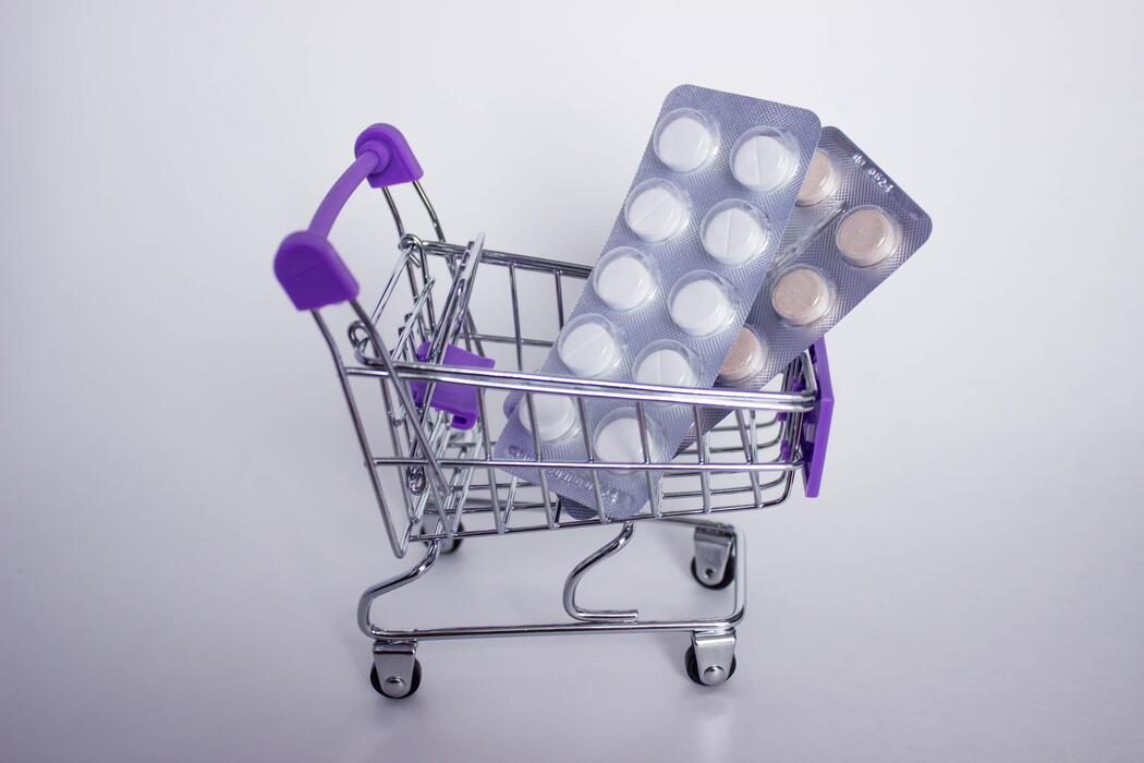viagra pills online - Mini decorative shopping cart with two blisters of tablets on white background.