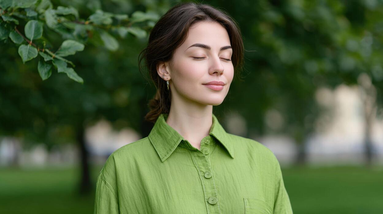 How to reduce anxiety immediately - Young woman in a green shirt enjoying nature with closed eyes, peaceful expression and serene surroundings in a park setting