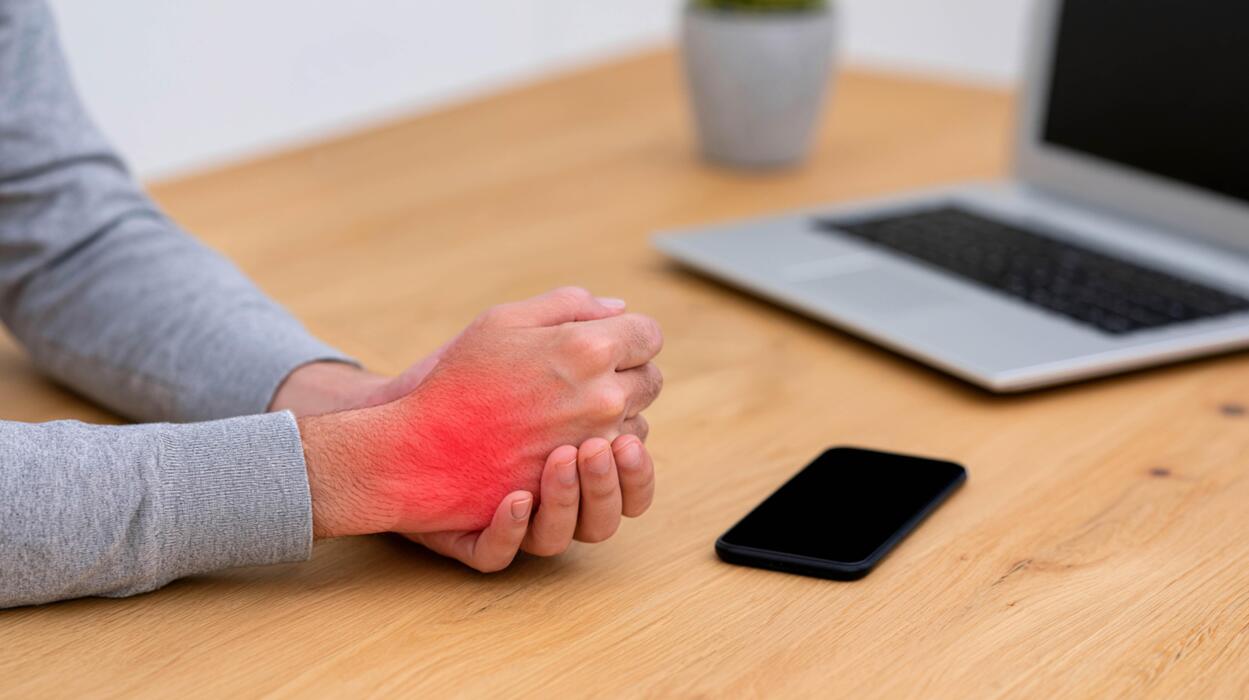 What are 5 symptoms of shingles? - Hand Gripping Inflamed Wrist with Red Pain Effect by Keyboard and Smartphone