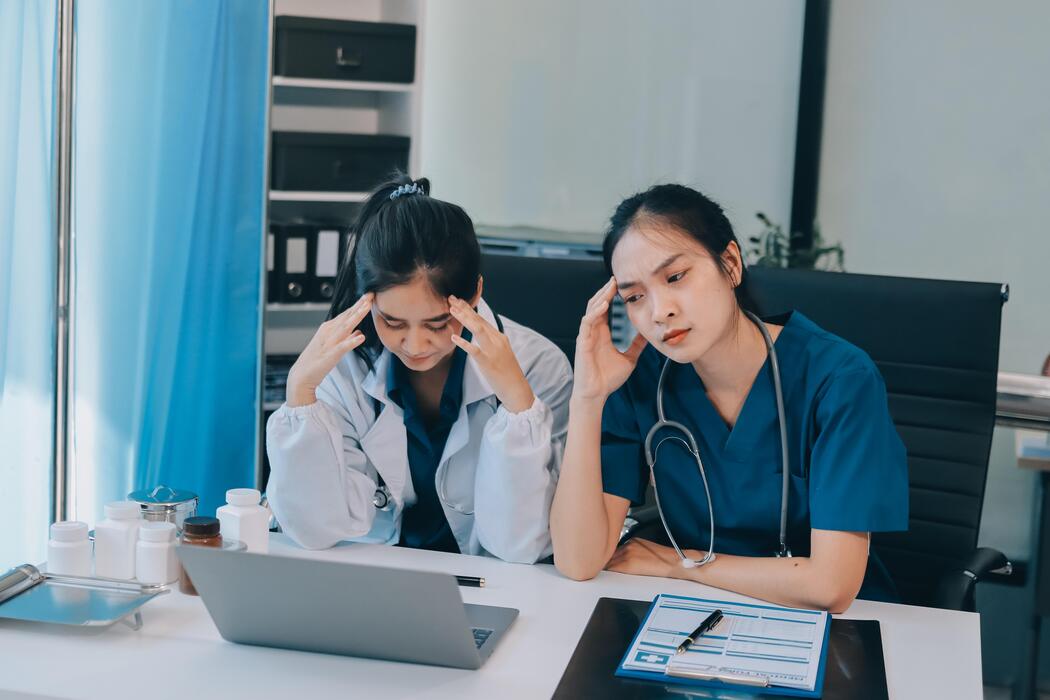 how to fall asleep faster with insomnia - Two women in scrubs sitting at a desk with laptops