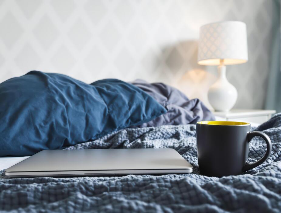 how to fall asleep faster reddit - A relaxing morning setup featuring a laptop and a dark mug on a messy bed, perfect for a remote workstation or a cozy nook. This sleepy setup includes soft bedding and a glowing lamp.