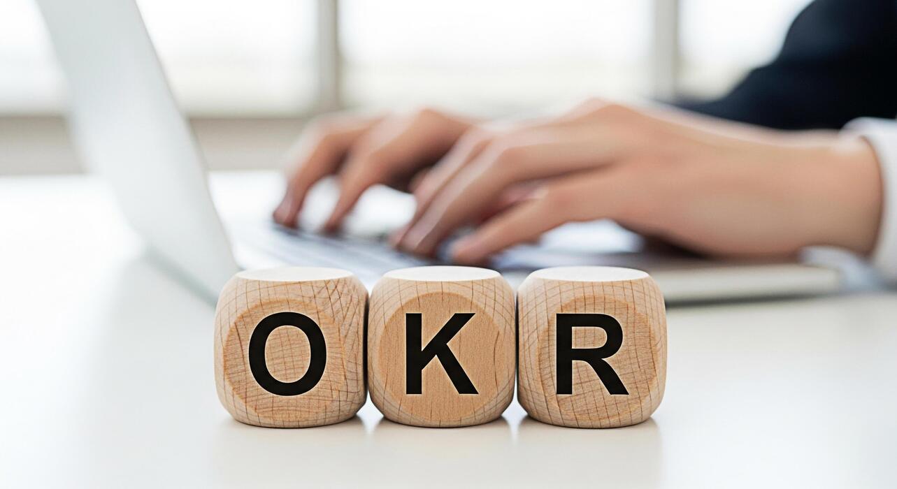 small business website design uk - Hands typing on a laptop with wooden blocks displaying OKR on a white desk symbolizing Objectives and Key Results in a bright office environment representing business strategy and goal setting