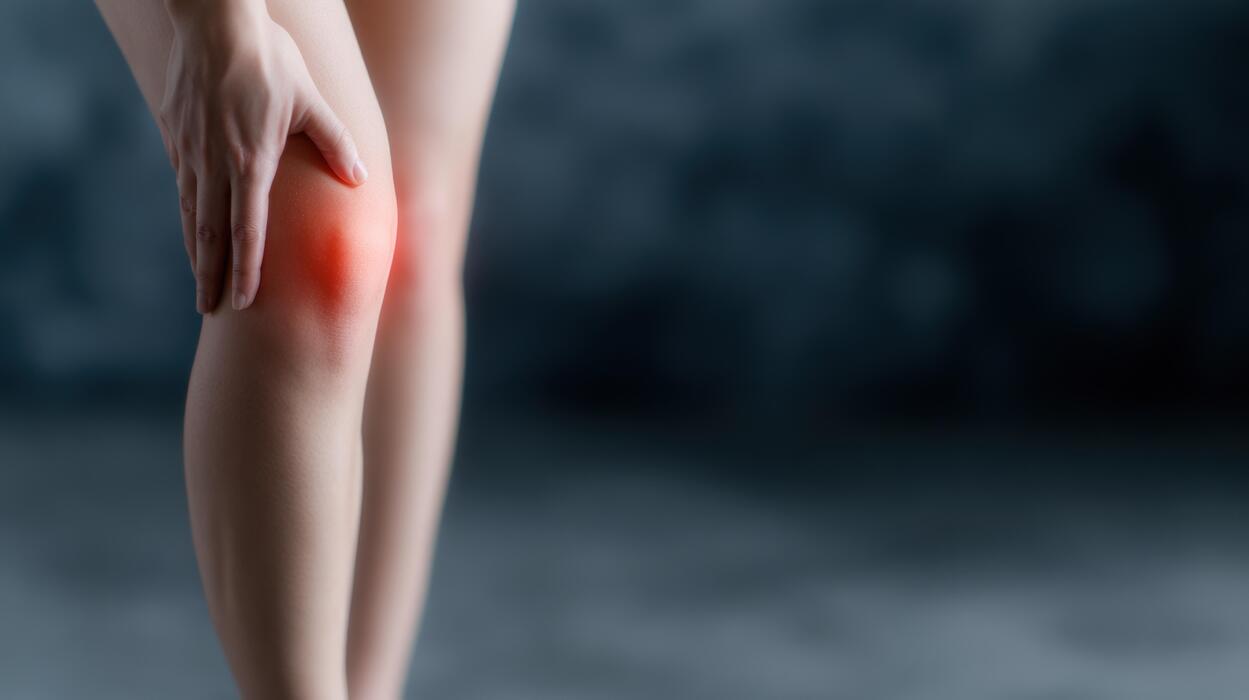 What is the best peptide for pain relief? - Human leg with hand touching painful knee joint displaying red inflammation spot on dark background for medical health and body care concept
